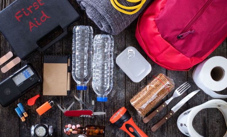 Seventy-two hour kit unpacked on a table: first aid manual, water bottles, medication and cutlery
