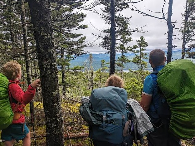 Three hikers with loaded packs stopping to look out over a lake