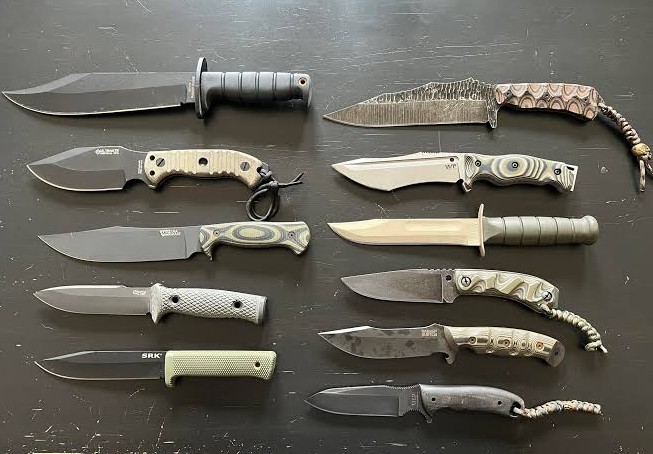 Ten fixed blade knives laid side by side to compare steel, grind and handle material