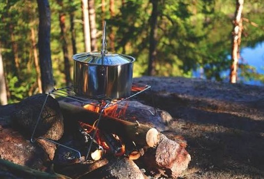 Cooking pot hanging from a tripod over an open fire at a lakeside camp
