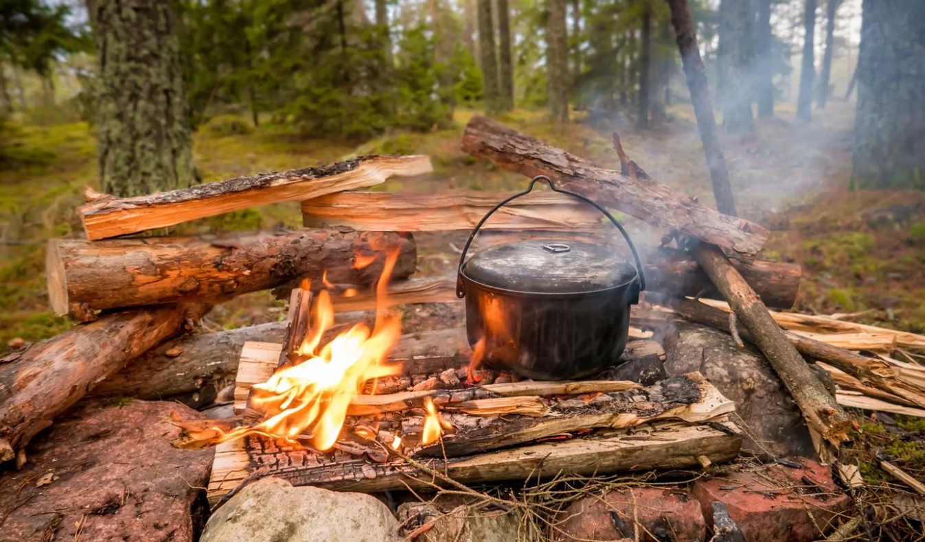 Cast iron pot suspended over an open campfire built from split logs